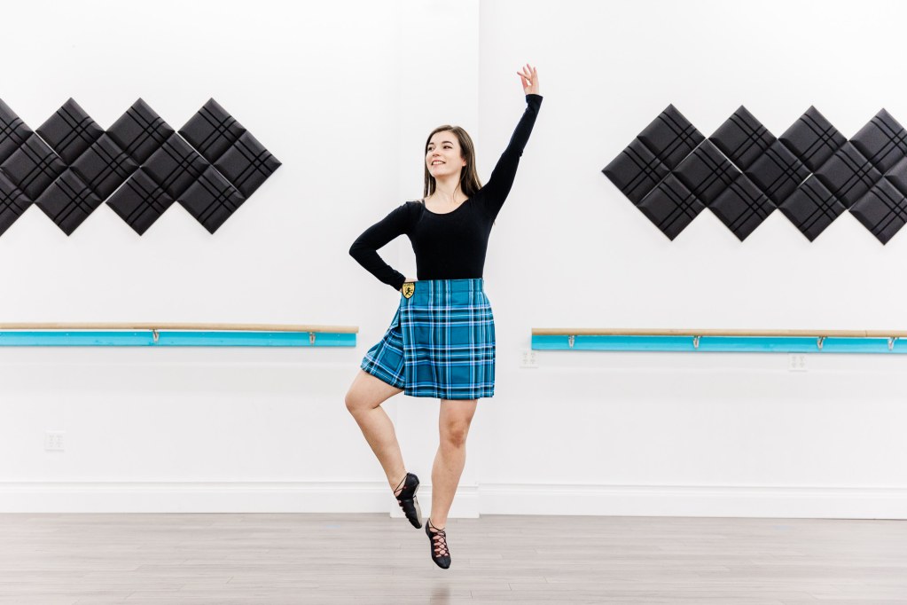A woman in a blue kilt does a jump