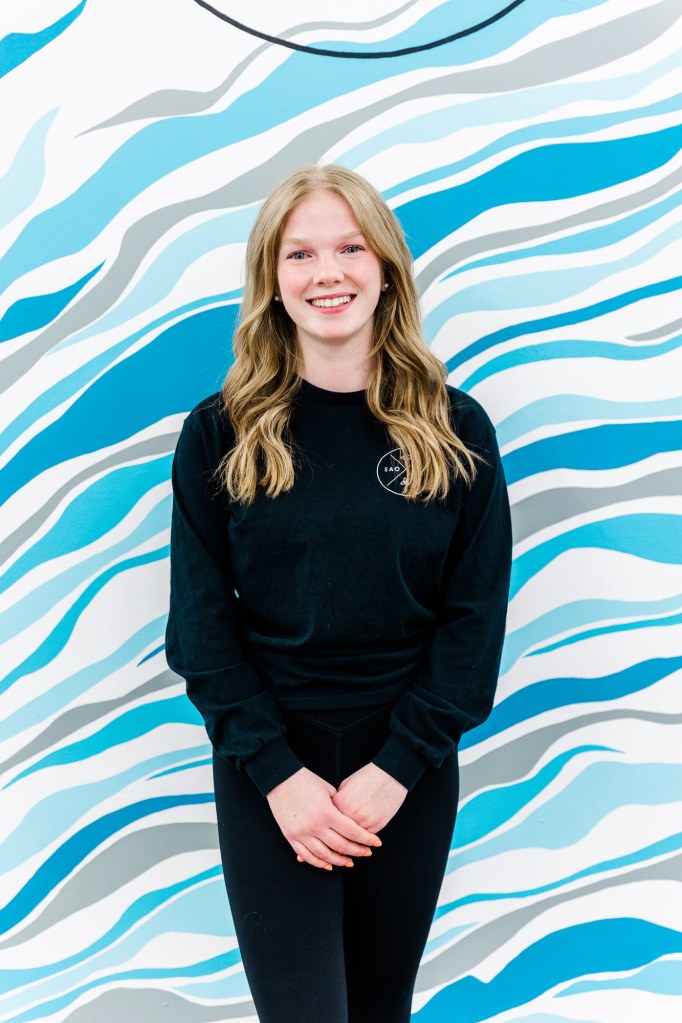 A woman in black smiling in front of a blue and white wall