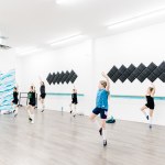 A children's dance class with 6 participants does a dance in a large white studio