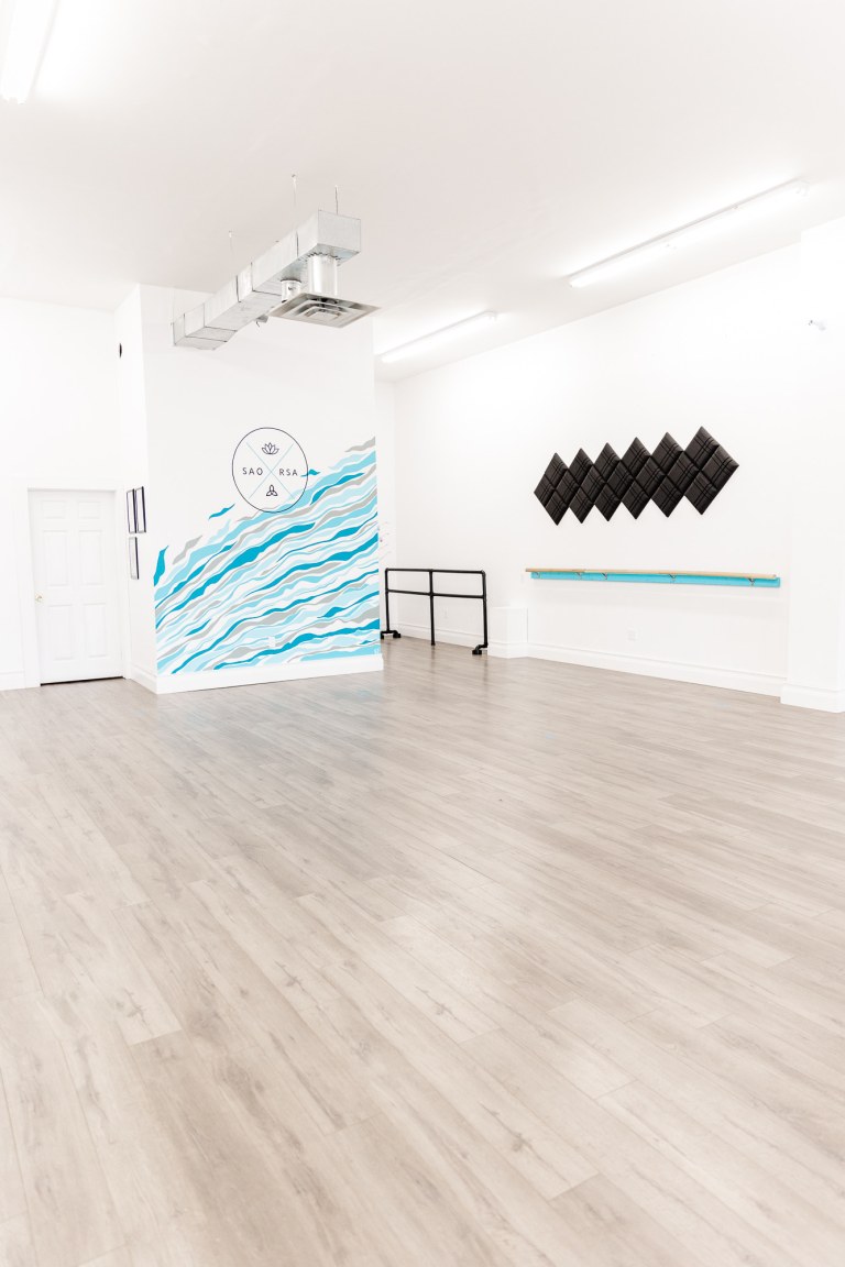 A large white room with wood flooring and a blue wall that reads "SAORSA"