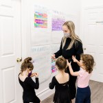 Three children stand with a woman wearing black in a hallway