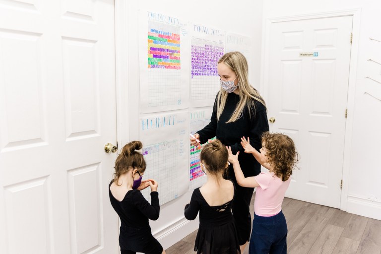 Three children stand with a woman wearing black in a hallway
