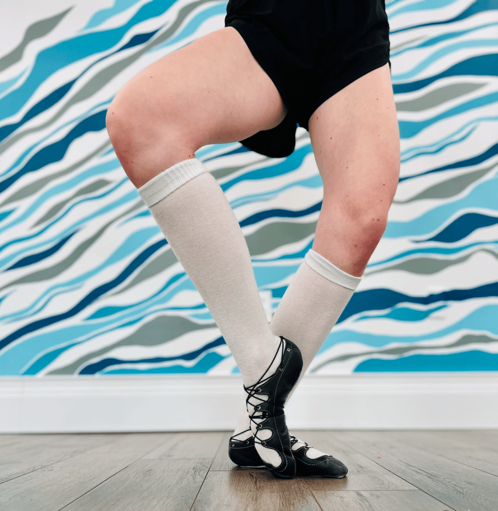 Legs of a highland dancer wearing white knee socks in front of a blue and white wall