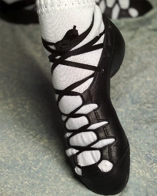 A pointed foot wearing white socks and a black leather dance shoe