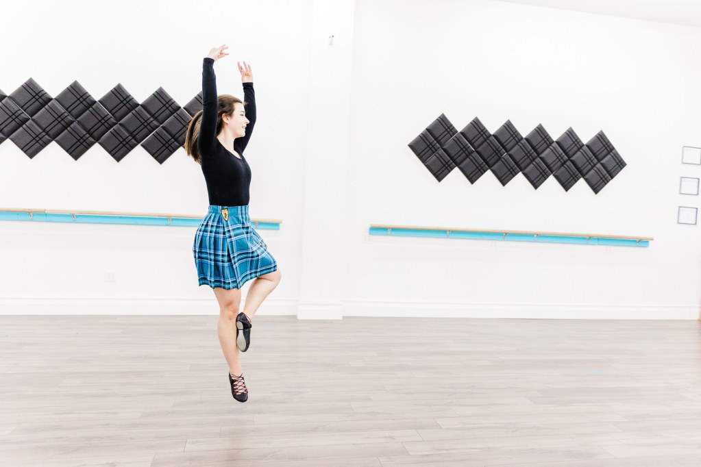 A dancer in a blue kilt does a jump in a white room