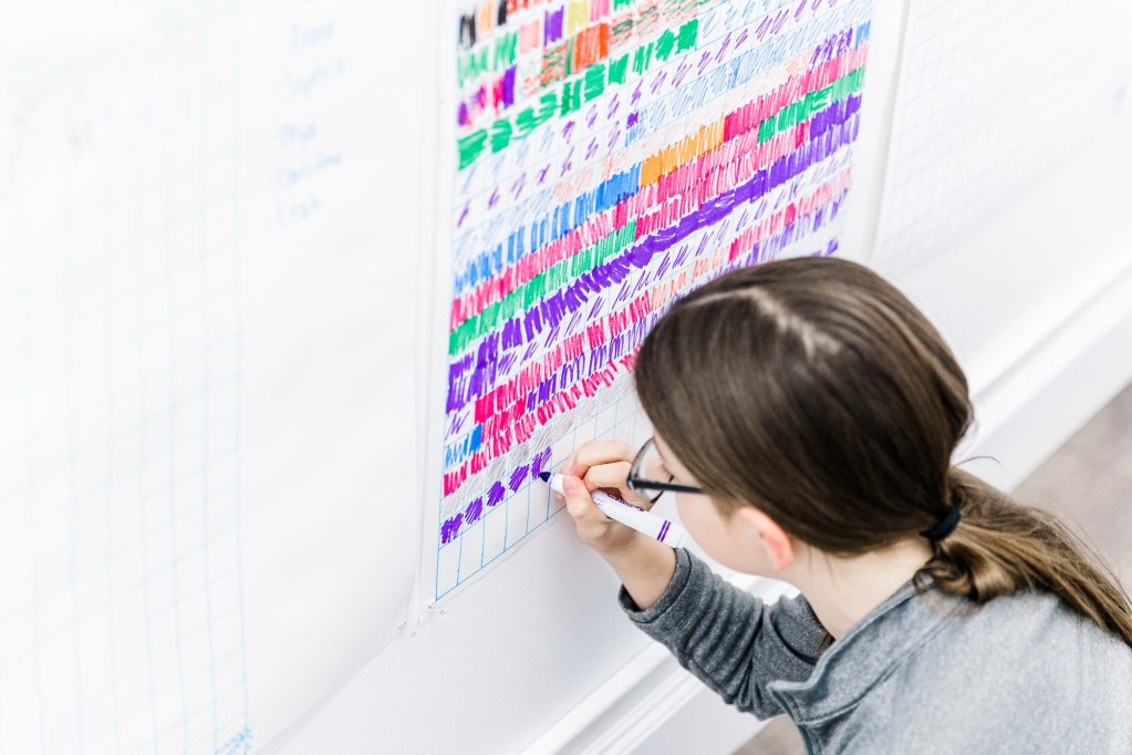 A girl colours in a purple square on a grid on the wall