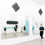 A woman in black instructs a childrens dance class in a white room