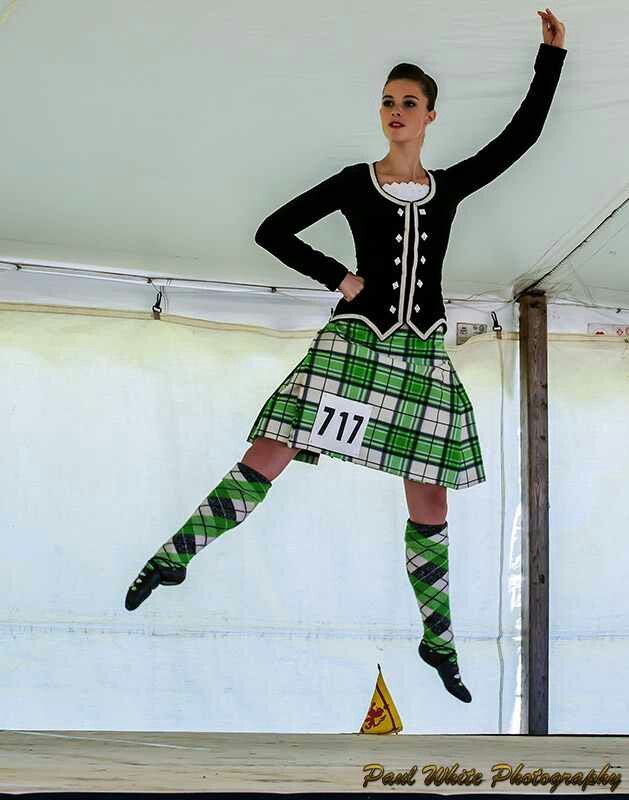A dancer in a green kilt and black jacket jumping on stage