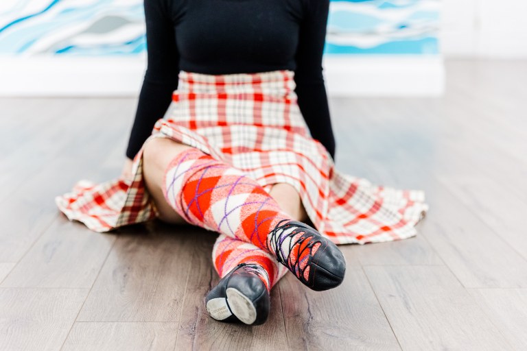 A dancer's legs in a read kilt with black dance shoes and red socks
