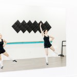 2 highland dancers in black jump and pose in a white room seen through a mirror