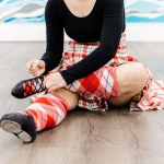 A dancer in a red kilt ties their black dance shoe