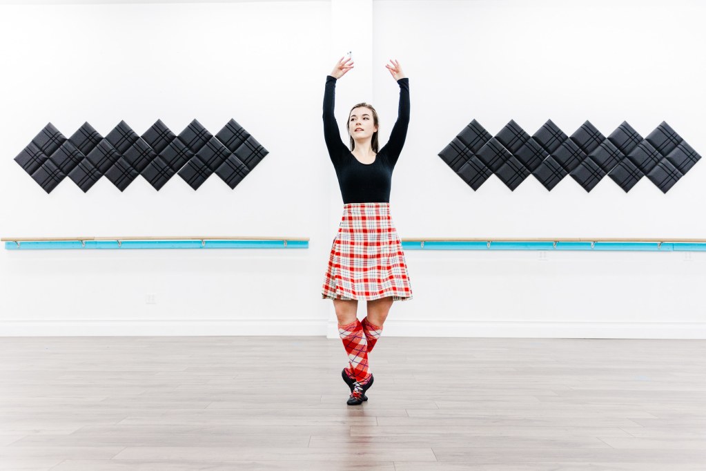 A dancer in a red kilt poses in a white room