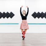 A dancer in a red kilt poses in a white room