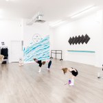 A children's dance class in a white room with a blue wall that reads "SAORSA"