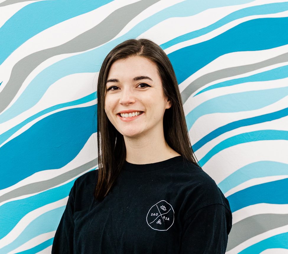 A woman wearing black smiles in front of a white and blue wall