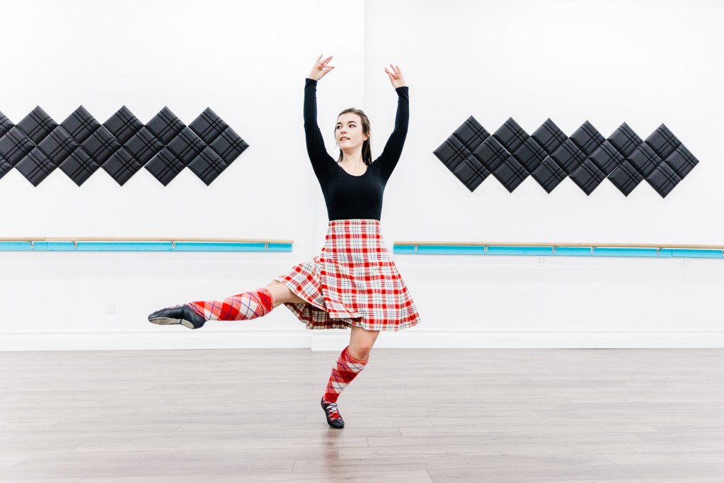 A dancer in a red kilt poses in a white room
