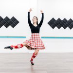 A dancer in a red kilt poses in a white room