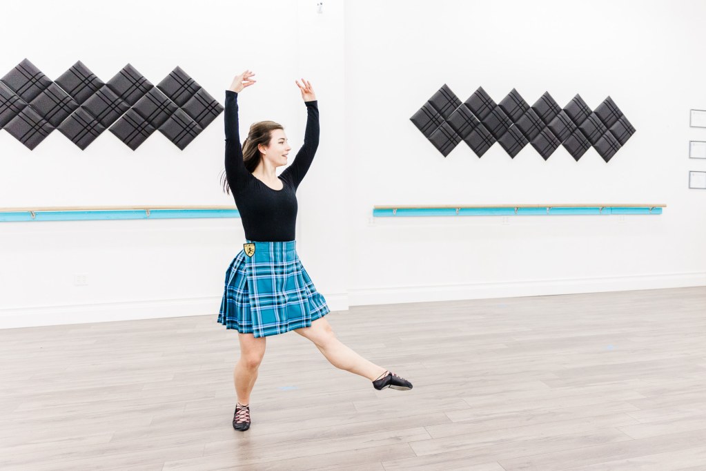 A woman dances wearing a black top and a blue skirt in a white room