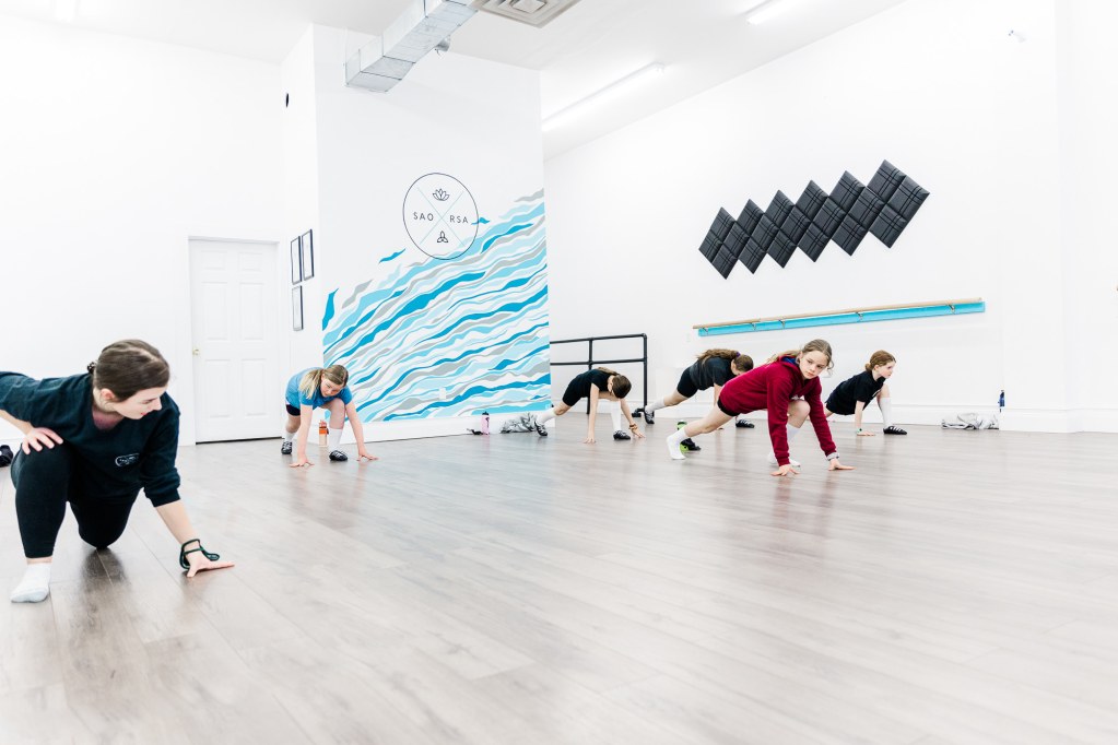 Dancers and instructor stretch in a white room