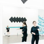 A dance instructor leads a class in a white room