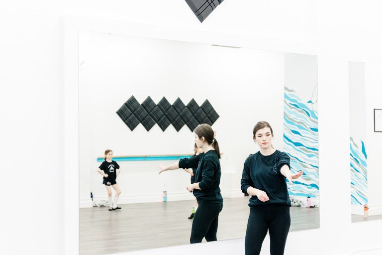 A dance instructor leads a class in a white room
