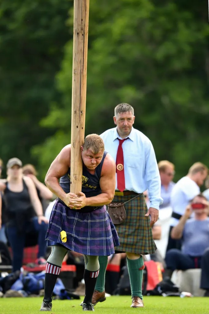 A man in a kilt holds a wooden pole