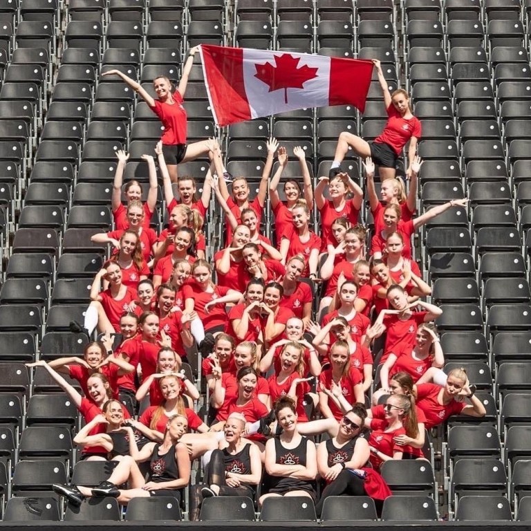 Women in red t shirts sit in arena stands and hold a canadian flag