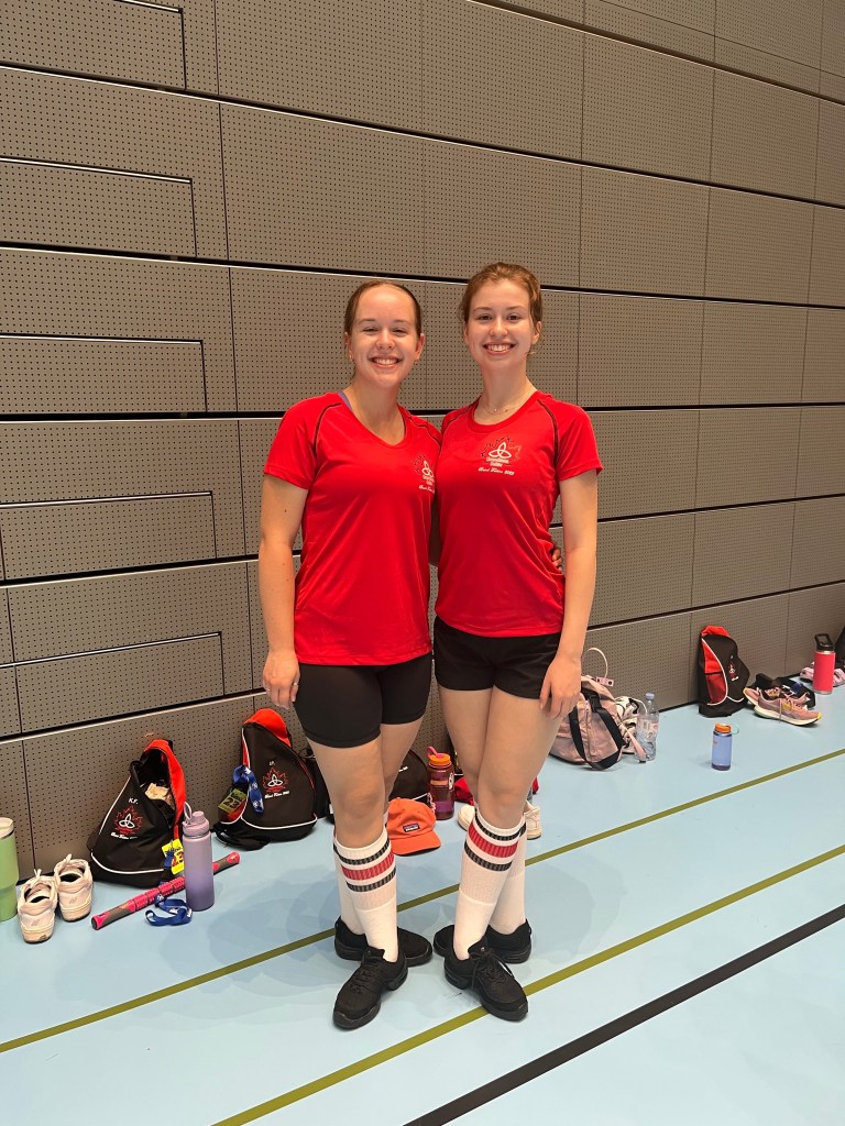 Two women in red shirts and black shorts smile