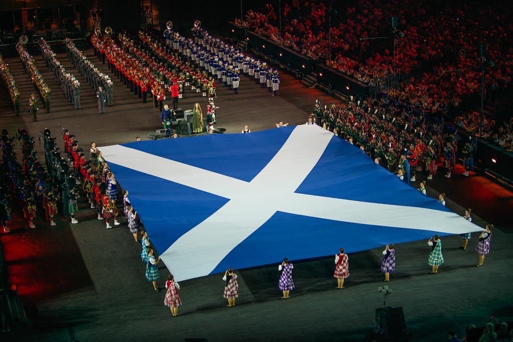 A large Scottish flag held on all sides by women in plaid outfits
