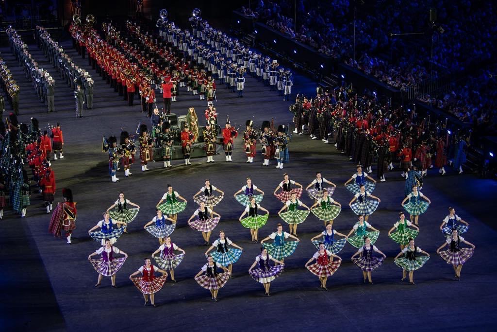 Dancers in multicolour dresses in line formations on a large stage