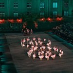 An arena with many dancers wearing white dresses in a circle formation with crowd on either side