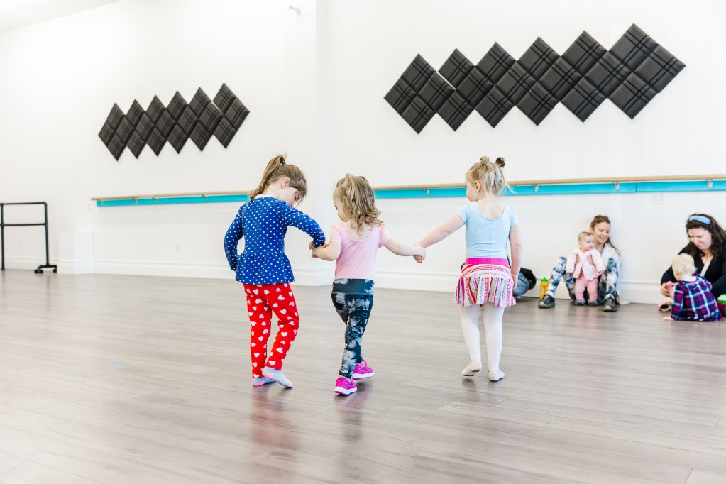 3 toddlers hold hands in a white room