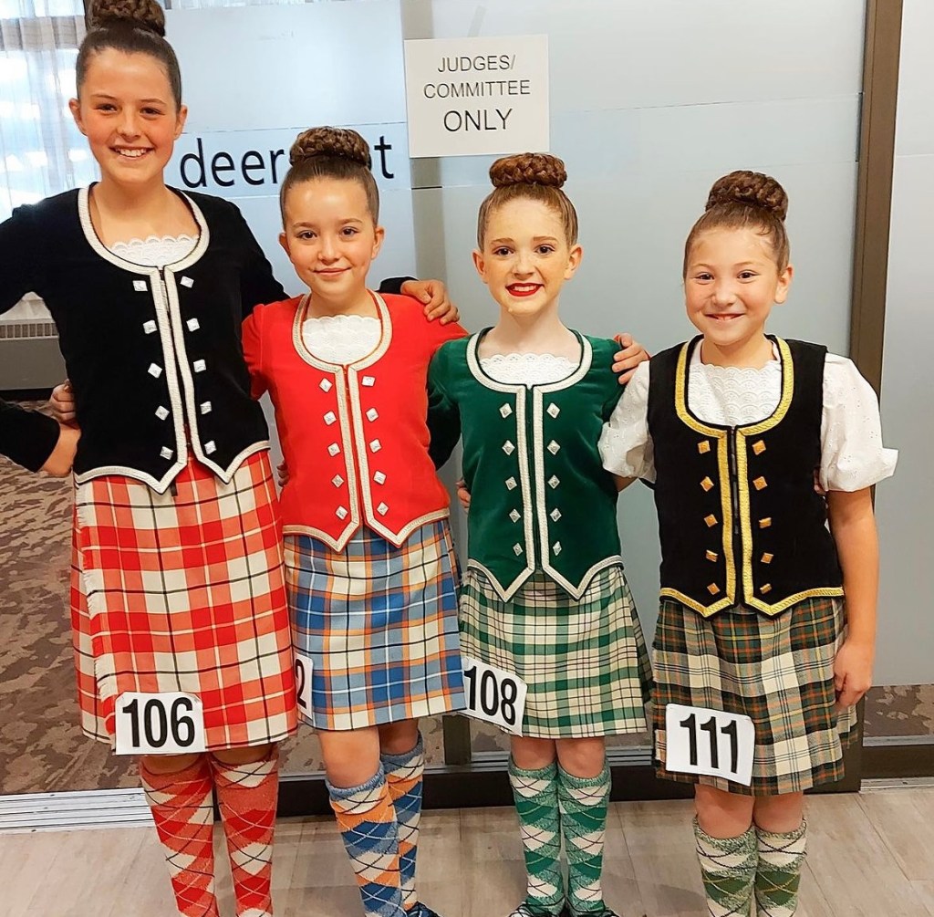 4 young girls smile wearing kilts