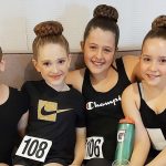 4 young girls wearing black smile on a couch