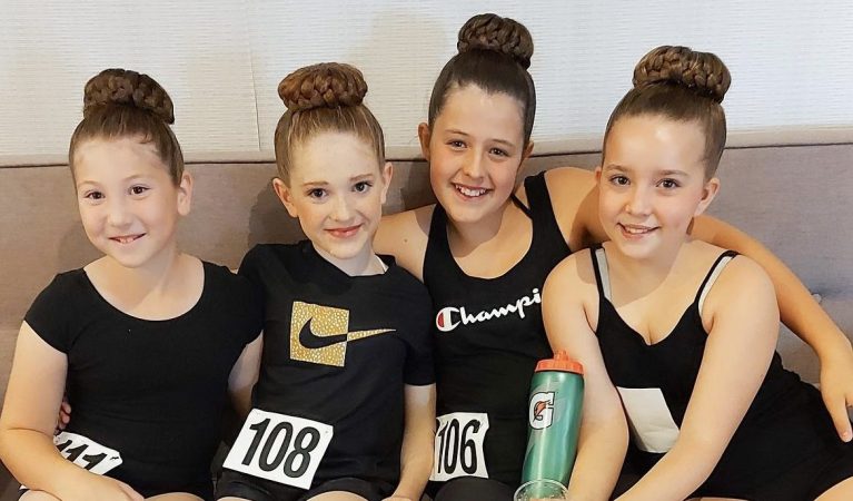 4 young girls wearing black smile on a couch