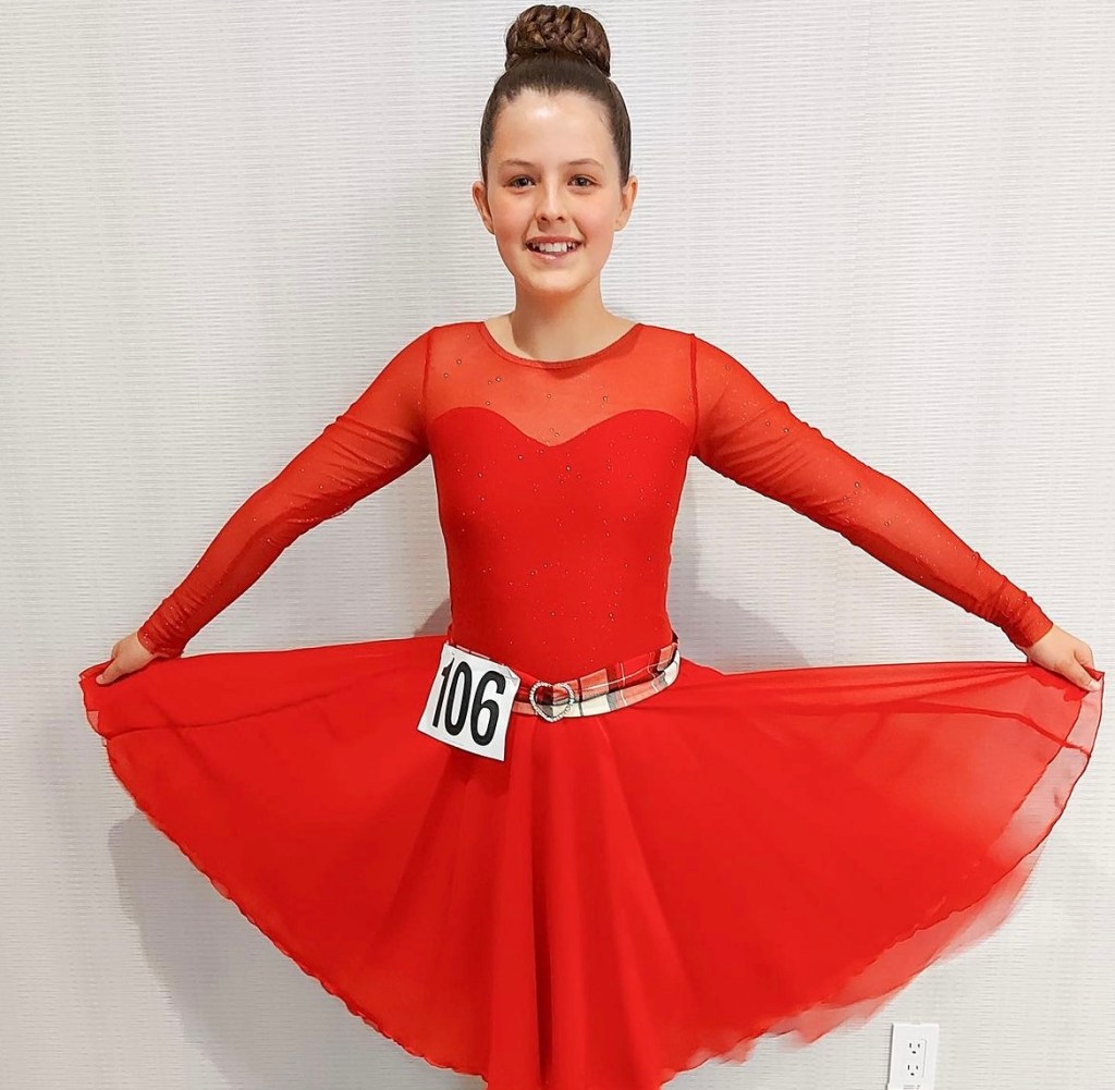A young dancer smiles wearing a red dress