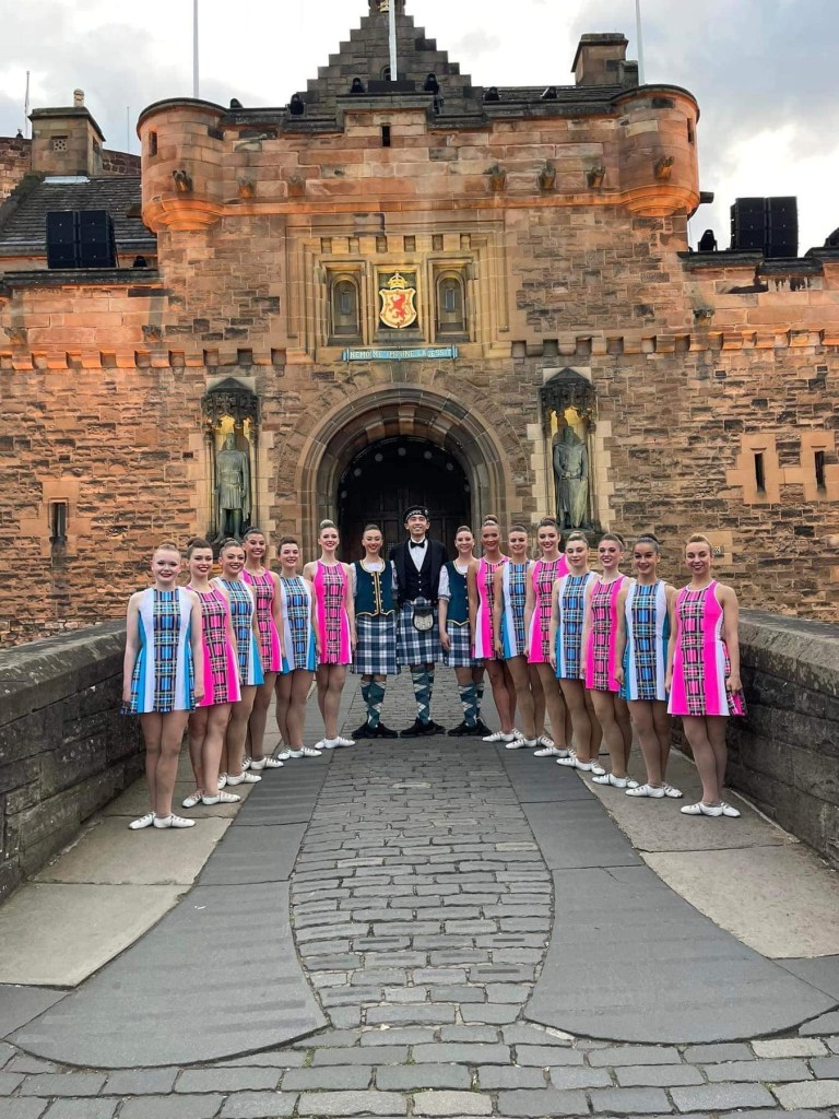 A large line of people pose in pink and blue dresses in front of a castle