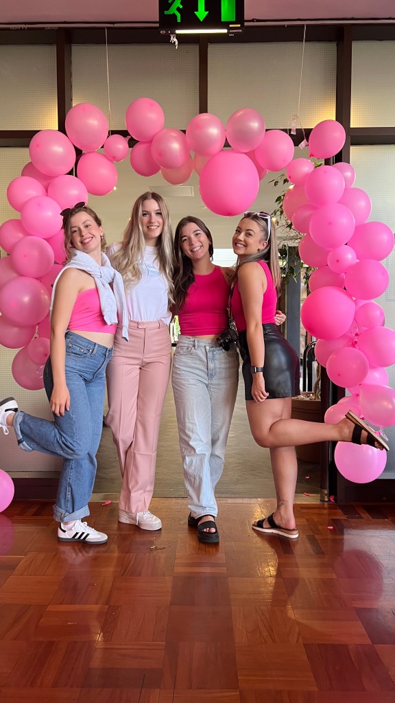 4 women wearing pink pose and smile