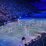 An area with a large crowd, and performers in a star formation on a large stage