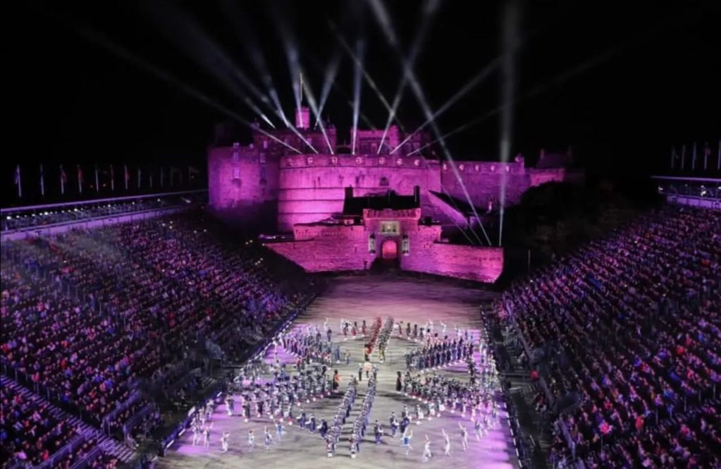 An area with a large crowd, fireworks in the background, and performers on a large stage