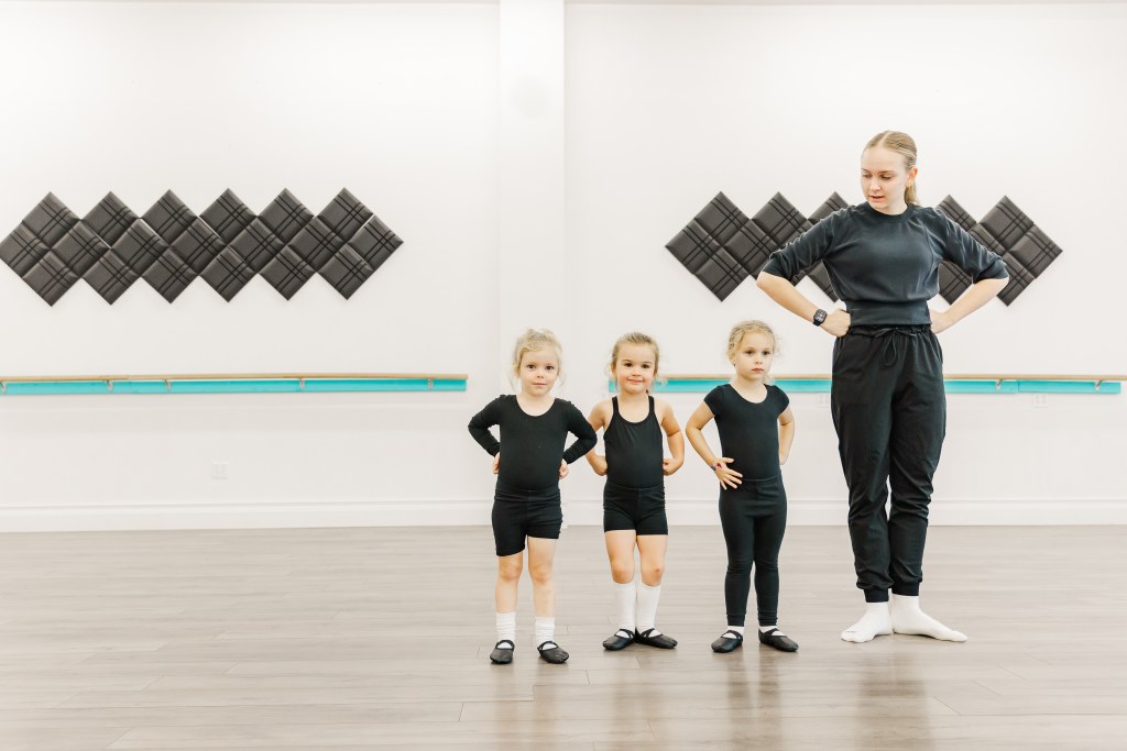 3 young dancers and a woman smile and pose in a white room
