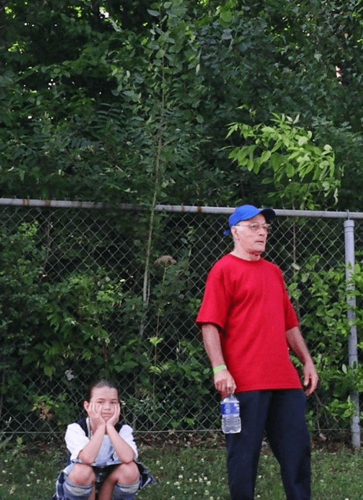 A man in a red shirt and blue hat next to a child in a kilt