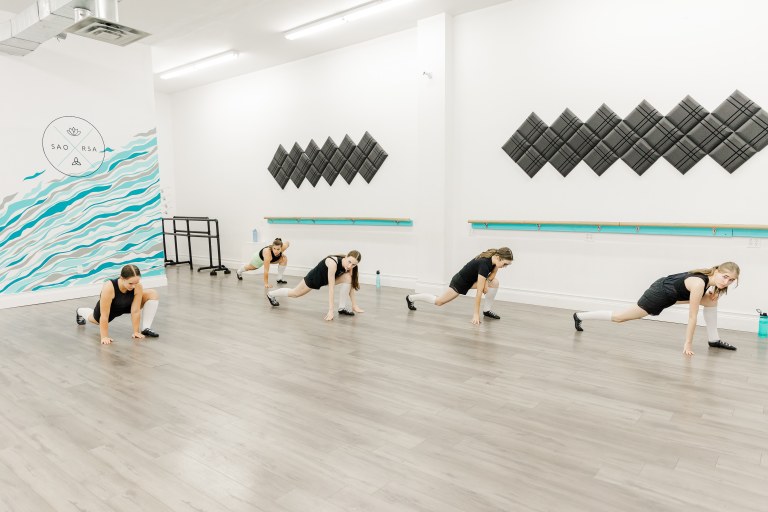 A group of 5 dancers stretch in a white room