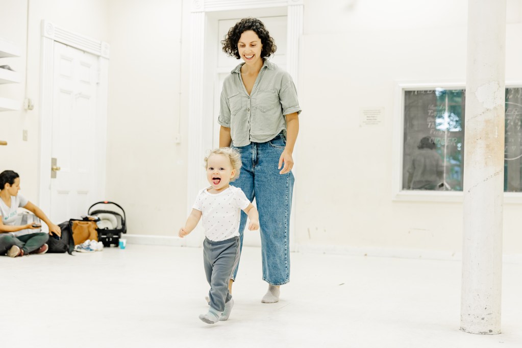 A mother and child smile and run in a white room