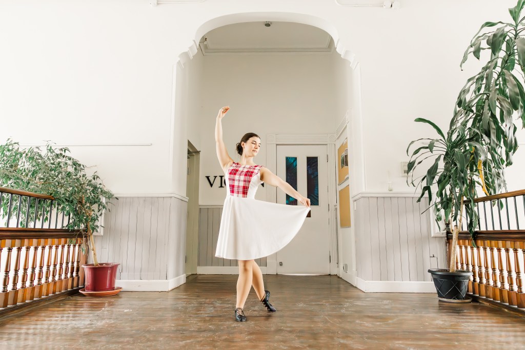 A dancer in a white and pink dress poses in a hallway