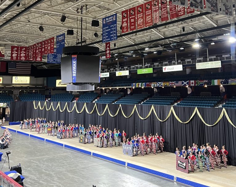 An arena with a large stage and highland dancers in kilts on it