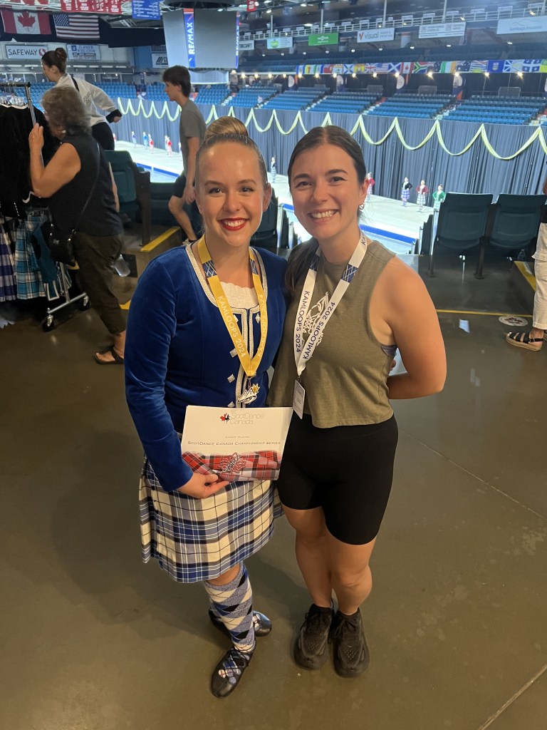 A highland dancer in a blue kilt stands with a woman in a green tank top