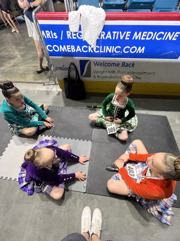 4 dancers in kilts sit on the ground stretching