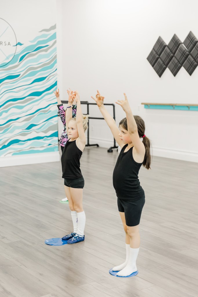 Two young dancers practice their poses in a white room