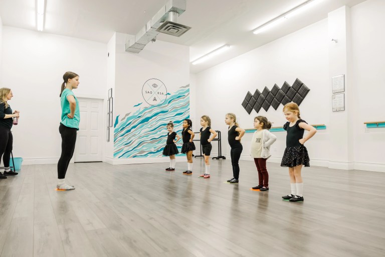 Young highland dancers stand in a line in a dance studio in a highland dance position. The white wall behind them reads "Saorsa". Saorsa Studio offers Highland Dance classes for ages 1 to adult in Fredericton, New Brunswick.